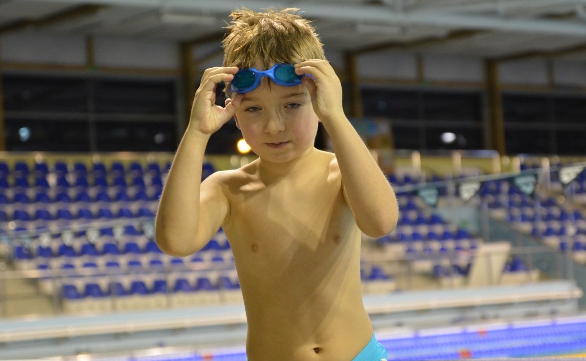 Chłopczyk na skraju basenu poprawiający okularki pływackie